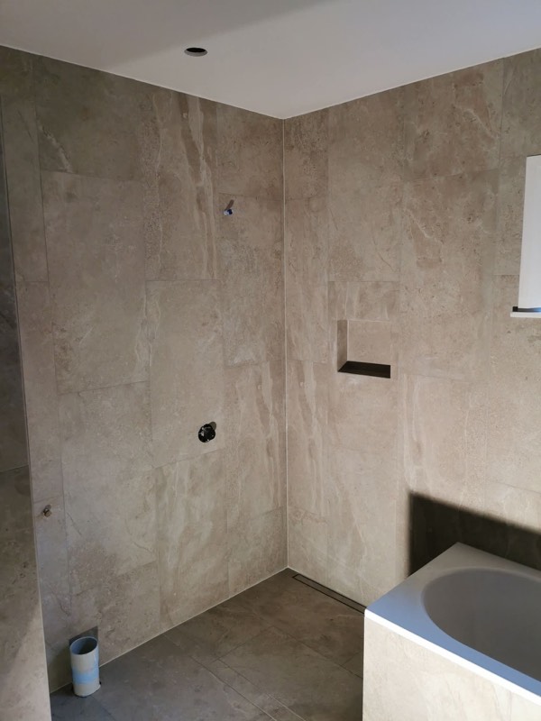 Large-format travertine-look bathroom wall tiles with a recessed niche and bath
