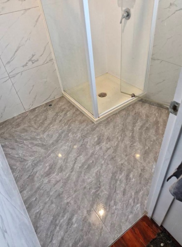 Marble-look tiled shower floor with white marble walls and glass screen