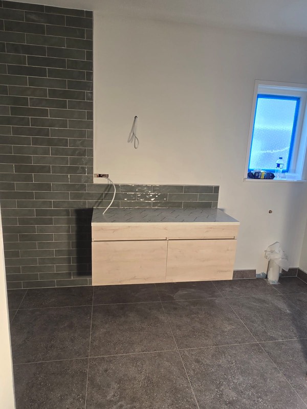 Laundry with a grey-green brick feature wall and dark floor tiles